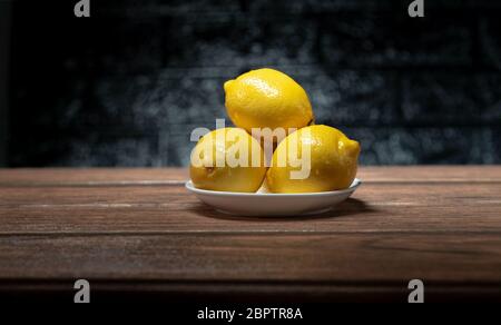 yellow lemon in a plate on a wooden table and dark ceramic type background Stock Photo
