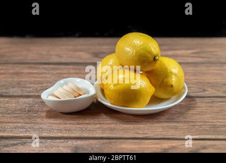 four fresh yellow lemons with vitamin c tablets on flat plates in a wood table dark food Stock Photo
