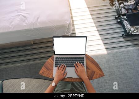 Top view mockup image of a woman using and typing on laptop with blank white desktop screen keyboard on wooden table next to the bed Stock Photo