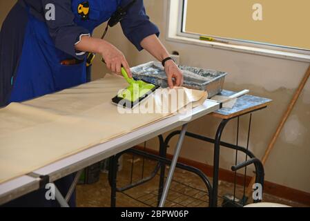 A woman spreads glue on the back of wallpaper, ready to decorate a bedroom Stock Photo