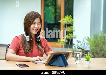Asian business woman using technology tablet with keyboard and headphone for working from home in outdoor home and garden, startups and business owner Stock Photo