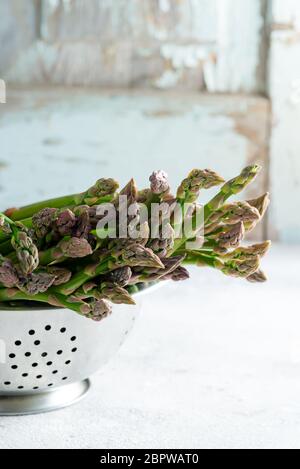 Raw organic asparagus in a colander ready for cooking healthy vegan food on a light grey marble background. Stock Photo