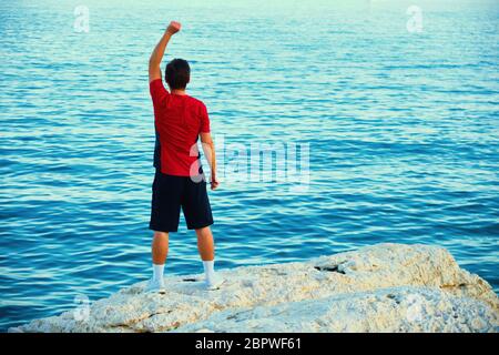 Man is doing exercises on the sea rock in the morning. Stock Photo