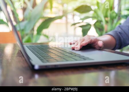 Closeup image of hand using and touching on laptop touchpad on wooden table Stock Photo