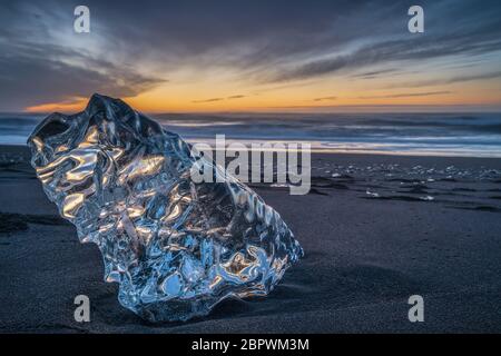 A big block of ice on the beach at sunrise, near the Jokulsarlon lagoon in South Iceland, also called Diamond beach