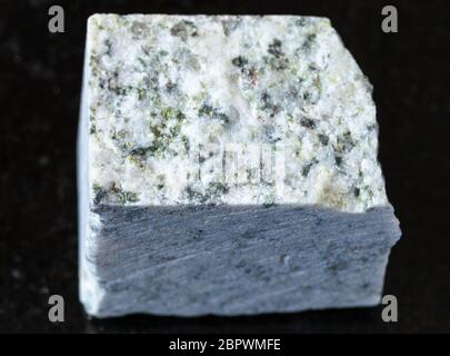 closeup of sample of natural mineral from geological collection - raw white Granite rock on black granite background Stock Photo