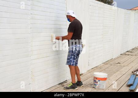 A worker paints with the white color a wall of a cabin of the lido before the reopening of the beach to customers for the new summer season. Stock Photo