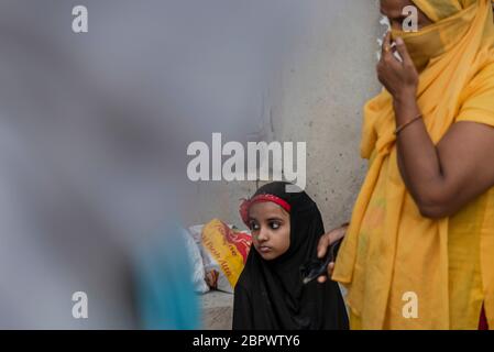 A young kid wait to receive free food with her mother in the Mustafabad area which was recently affected by riots, as the country relaxed its lockdown restriction on May 14, 2020 in New Delhi, India. The Mustafabad area was among the worst affected areas as riots broke out in India's national capital in February over a controversial citizenship amendment law passed by the Bharatiya Janata Party government. Several families which were left homeless due to arson by rioters are now taking care of themselves amid a nationwide lockdown imposed by the government to curb the spread of coronavirus in Stock Photo