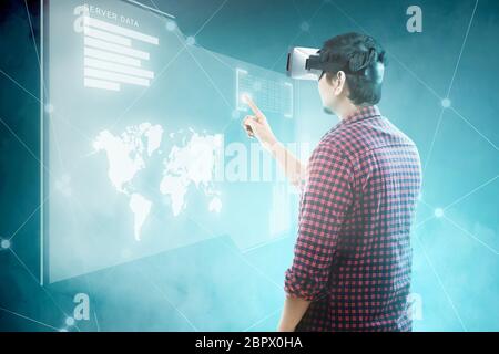 Rear view of asian man touching binary code on digital interface with virtual reality device display the world map, graphic bar and binary code. Augme Stock Photo