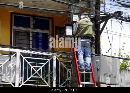 Antipolo City, Philippines - May 16, 2020: Employee of a telecommunication company works on a set of cables at a pole. Stock Photo