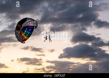 people ride, fly on a parachute along the coast over the sea against the background of a wonderful sunset. Attraction entertainment for tourists in th Stock Photo