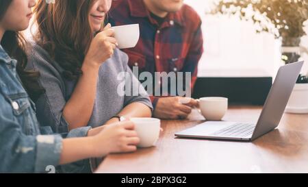 Three young asian people drinking coffee while using and looking at the same laptop computer Stock Photo