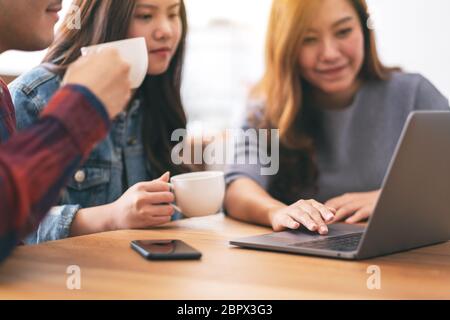 Three young asian people drinking coffee while using and looking at the same laptop computer Stock Photo