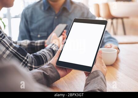 A woman using and looking at mockup tablet pc on wooden table with friends in background Stock Photo