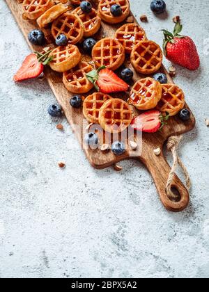 Small round delicious soft belgian waffles on cutting board. Fresh belgian waffles with berries and caramel sauce top view. Copy space for text or moc Stock Photo