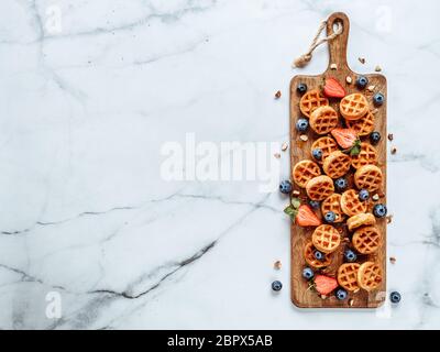 Small round delicious soft belgian waffles on cutting board. Fresh belgian waffles with berries and caramel sauce top view. Copy space for text or moc Stock Photo