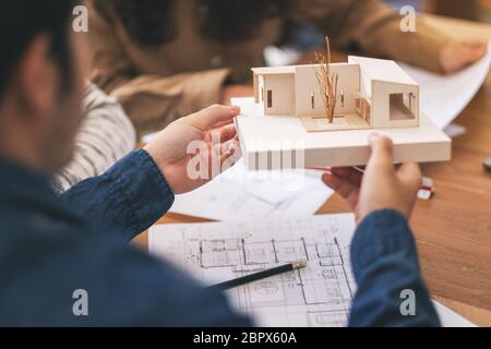 Group of an architect holding and discussing about an architecture model with shop drawing paper on table in office Stock Photo