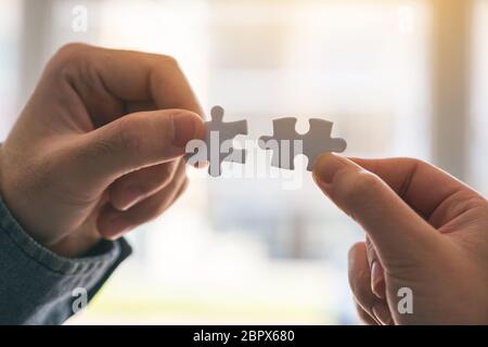 Closeup image of two hands holding and putting a piece of white jigsaw puzzle together Stock Photo