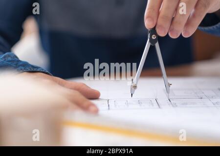 An architect using compass to draw and measure shop drawing in office Stock Photo