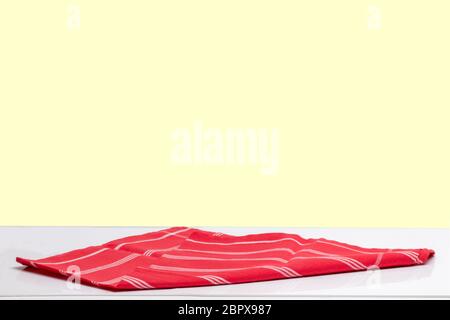 Closeup of a empty red striped tablecloth or napkin on a bright table against light yellow background. Template for your food and product display mont Stock Photo