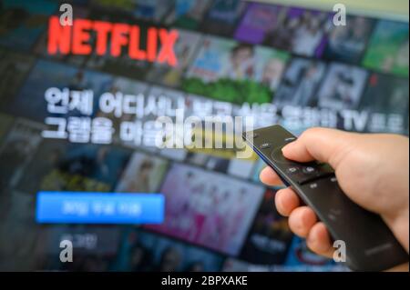 Seoul, South Korea - May 20, 2020: Man's hand operating remote control towards television with Netflix screen on. Stock Photo