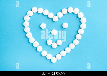 Heart shaped smile made from white medical pills on blue paper background. The concept of sedative drugs and recovery Stock Photo