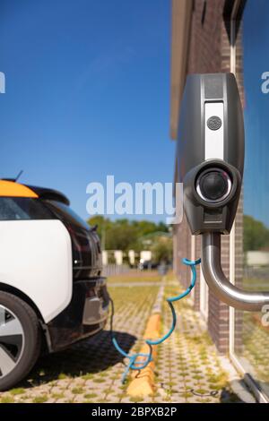An electric car being charged at a electronic car charging station on a sunny day in summer. New environmental friendly ways of using energy. Vertical Stock Photo