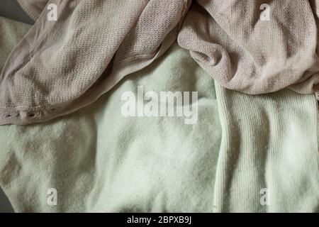 Old textiles from clothes in washed out pink and mintgreen colors laying on a pile. Worn pieces with holes, pills and fluffs in different materials re Stock Photo
