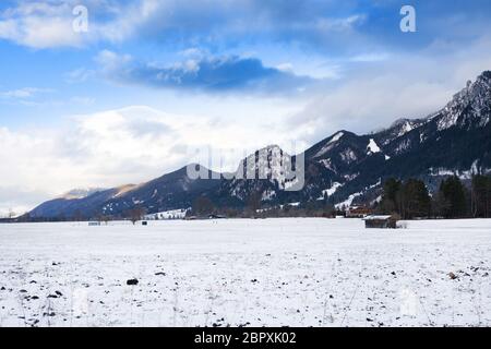 Wooden shed in snowy field against Alps in winter day. Schwangau, Bavaria, Germany Stock Photo
