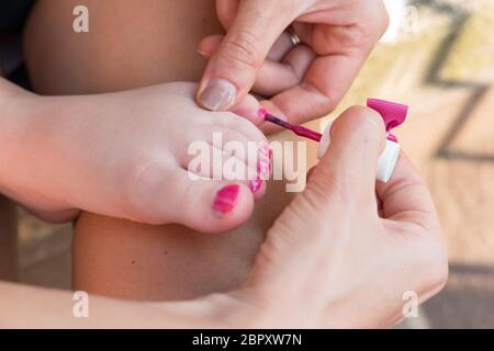 Mother painting nails of his little daughter. Fun activity at home, girl birthday party, spring and summertime. Stock Photo