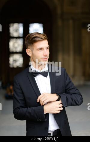 Young man standing and posing, wearing black suit and bow tie. Stock Photo