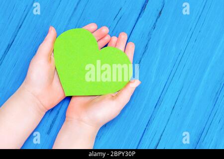 Top view of green heart in hands of child on wooden blue background. Copy space. Concept of environmental protection and Earth day. Stock Photo