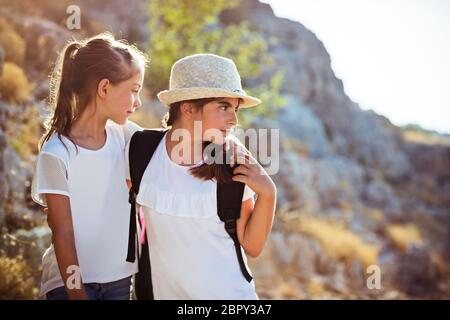 Two school girls with backpacks traveling along mountains, with pleasure spending time in a sportive summer camp Stock Photo