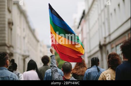 Rear view of people in the pride parade. Group of people on the city street with gay rainbow flag. Stock Photo