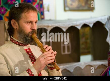 Slavic man plays an ethnic pipe. Belarusian musician in national clothes. Stock Photo