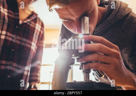 High school student using a microscope in a science class. Boy looking at slides through a microscope in biology class Stock Photo