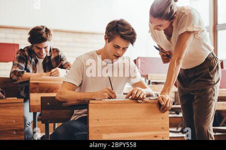 Female professor helping a student at classroom. Teacher assisting the problem of a student in her lecture. Stock Photo