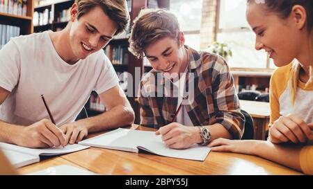 Group of students sitting at table in library and studying together. Happy young friends working on high school project. Stock Photo