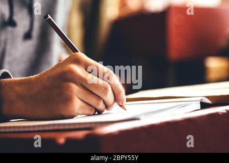 Close-up of a male student writing in a notebook. Boy studying in classroom writing in book with a pencil. Stock Photo
