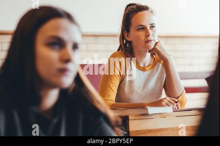 Beautiful girl sitting in class with classmates around paying attention to the lecture. Young people studying at the high school. Stock Photo