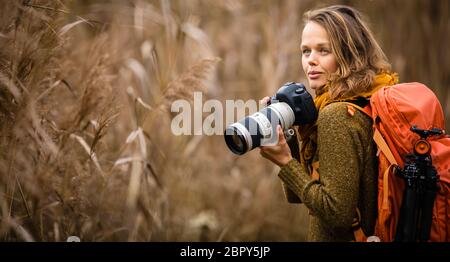 Pretty, female photographer taking pictures outdoor on a lovely autumn day - shallow DOF, color toned image
