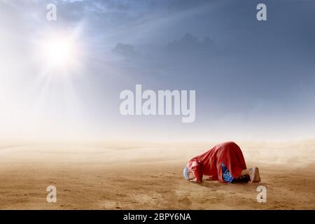 Rear view of asian muslim man praying in prostration position on desert with sun rays and dark sky background Stock Photo