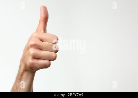 A male hand on a gray background holds a thumb up expressing Stock Photo