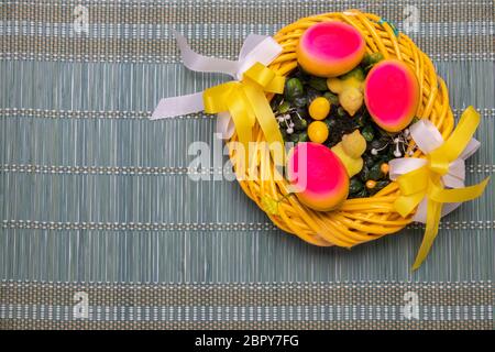 Easter decorations background. Closeup of a yellow Easter wreath with yellow little easter chicks and three easter eggs on a green bamboo straw mat. S Stock Photo