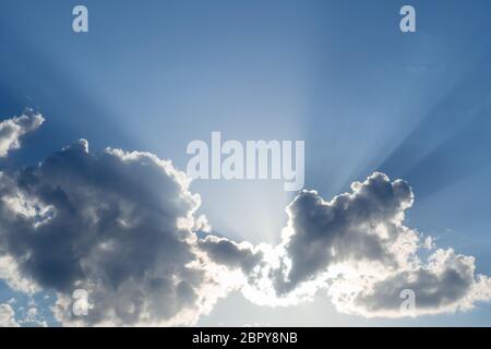 Sun shines behind the clouds, rays and shadows on blue sky. Copy space Stock Photo