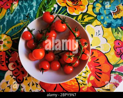High angle shot of cherry tomatoes in a white bowl on a colorful floral surface Stock Photo