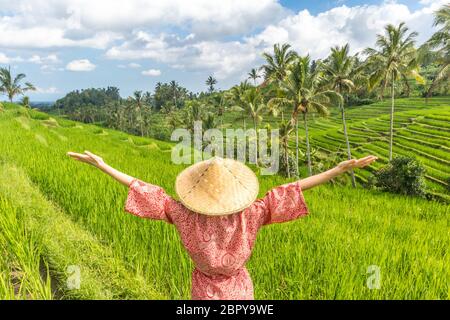 Relaxed fashionable caucasian woman wearing red asian style kimono and traditional asian paddy hat, arms rised to sky, enjoying pure nature at beautif Stock Photo