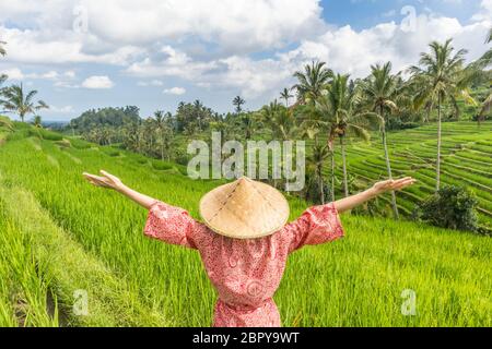 Relaxed fashionable caucasian woman wearing red asian style kimono and traditional asian paddy hat, arms rised to sky, enjoying pure nature at beautif Stock Photo