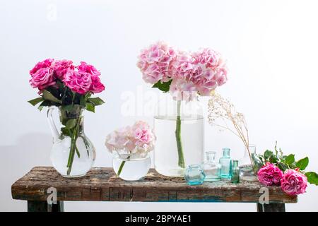 A bouquet of red roses in a tin bucket, multicolored pastel colored hydrangeas in a glass jar, gypsophila in a flask and a set of small bottles on the Stock Photo