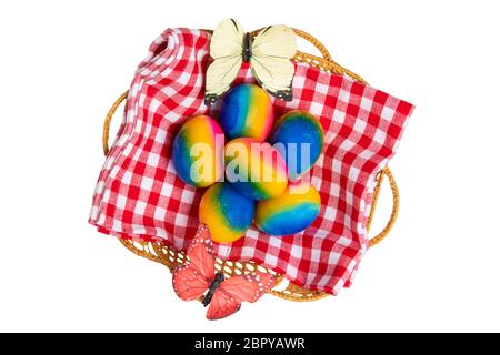 Happy easter decorations background. Top view of colorful easter eggs in a basket on red checkered napkin and two butterflies isolated on a white back Stock Photo